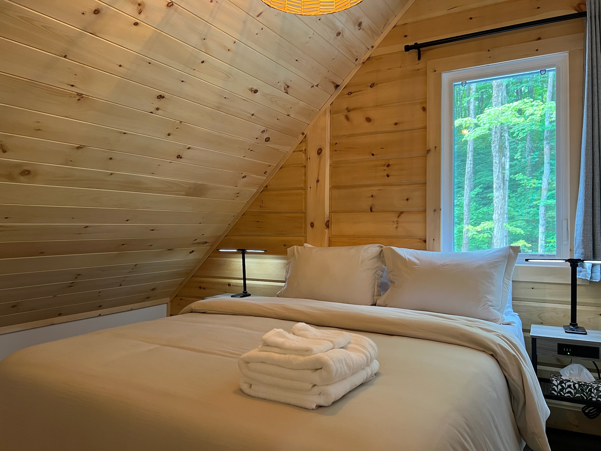 Chambre droite à l’étage sous le toit de bois avec vue sur la forêt