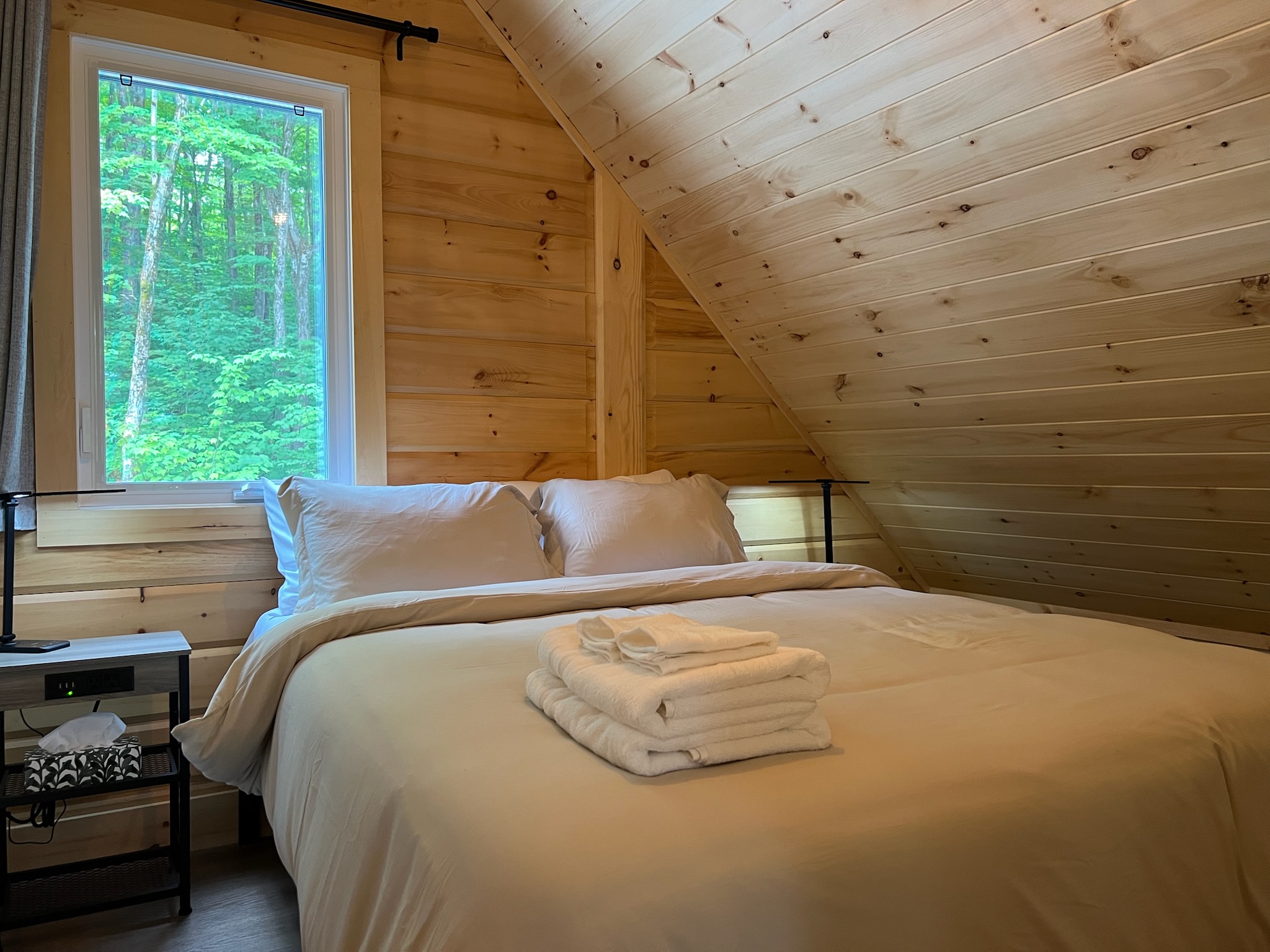 Chambre gauche à l’étage sous le toit de bois avec vue sur la forêt