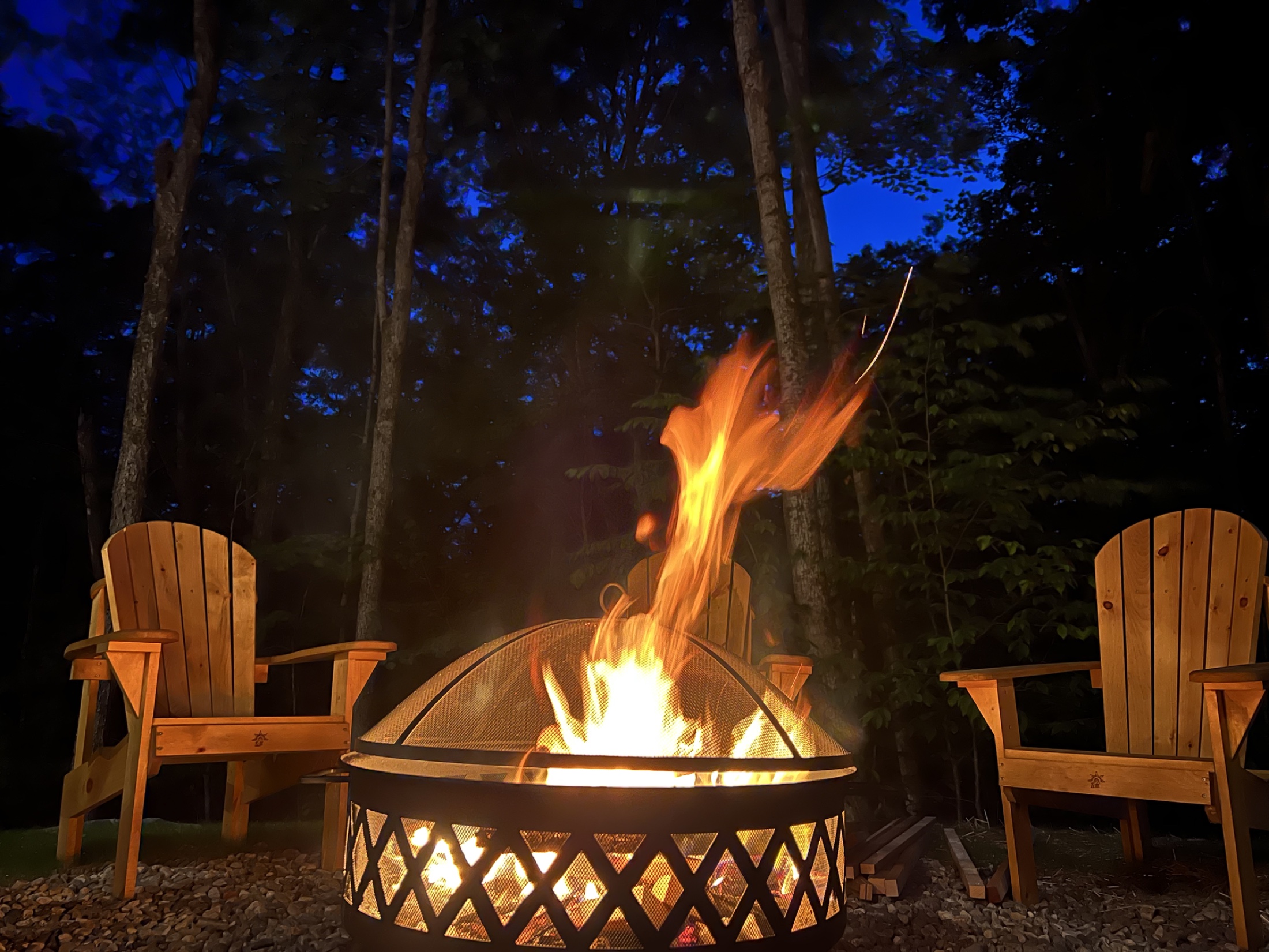 Feu de bois dans le foyer extérieur entouré de chaises Adirondack à la tombée de la nuit