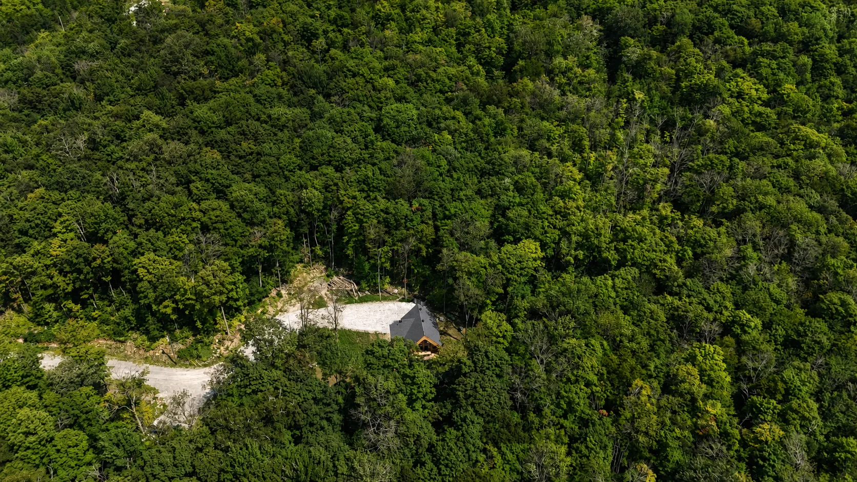 Vue aérienne éloignée montrant le chalet isolé au milieu de la forêt