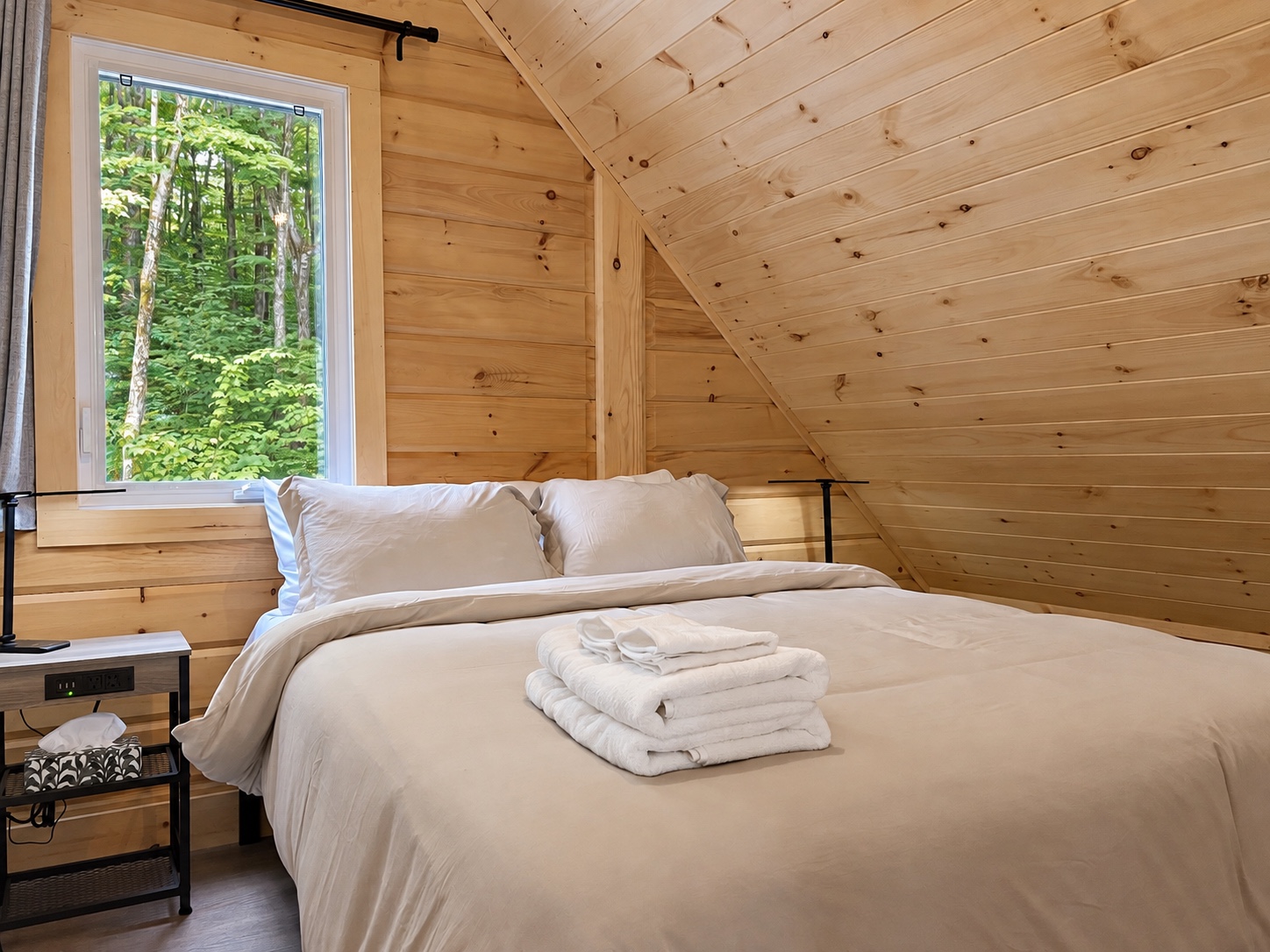 Chambre gauche à l’étage sous le toit de bois avec vue sur la forêt