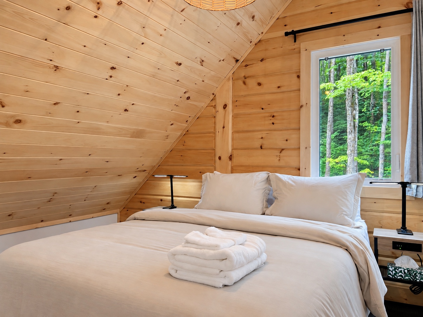 Chambre droite à l’étage sous le toit de bois avec vue sur la forêt