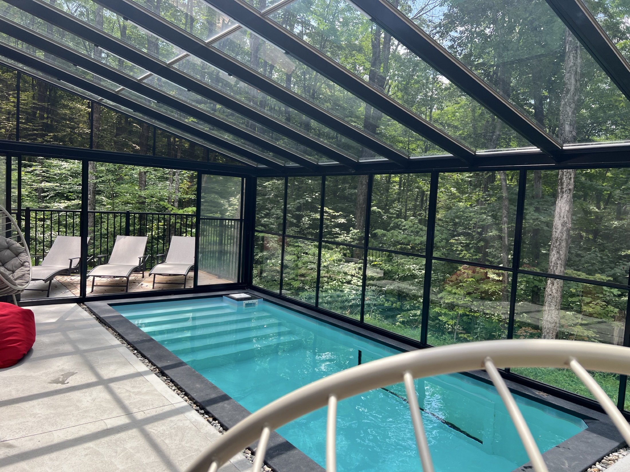 Piscine intérieure sous le solarium vitré avec vue sur la forêt en été