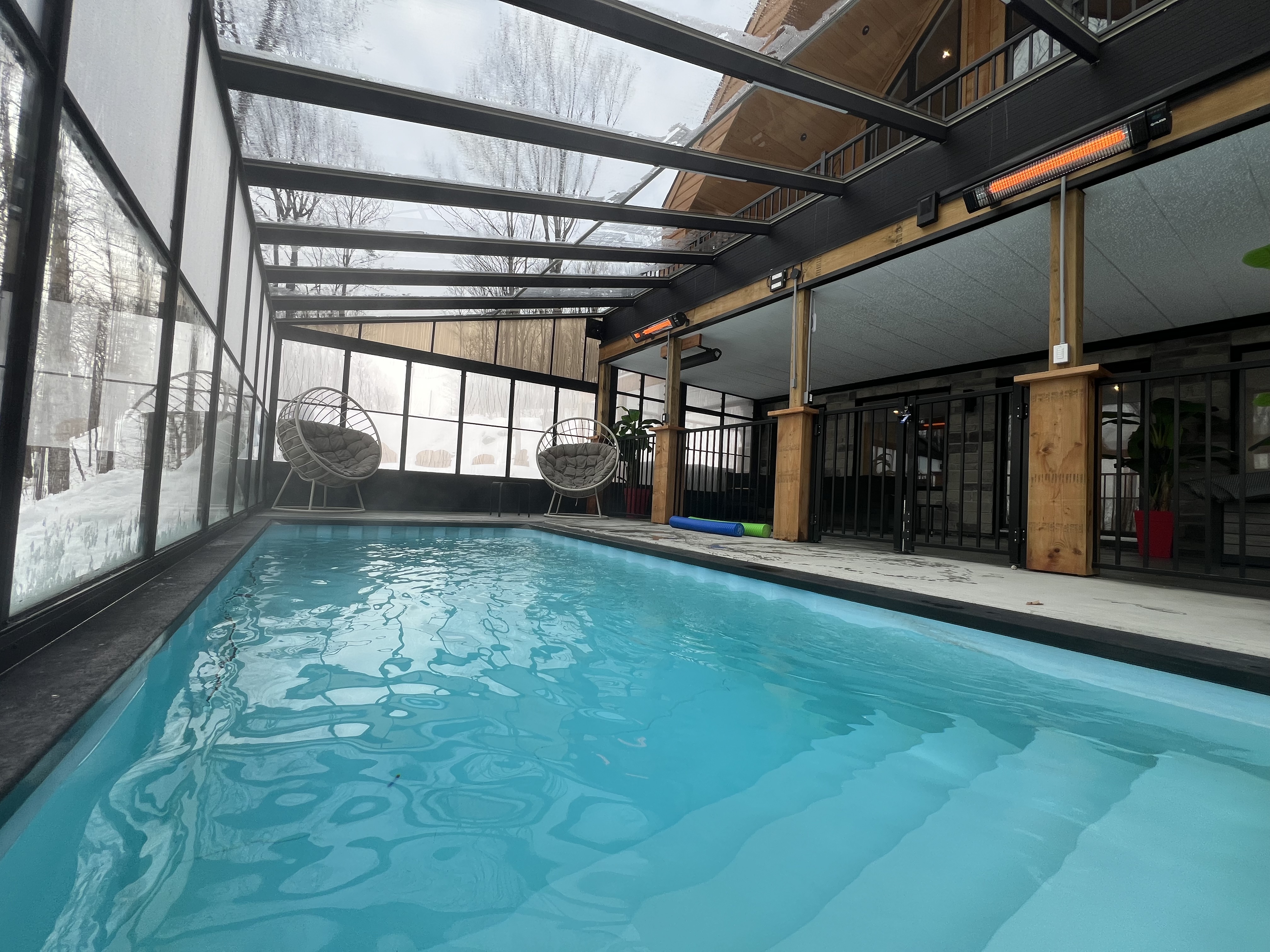 Piscine chauffée à l’intérieur du solarium avec la forêt enneigée visible à travers les murs vitrés