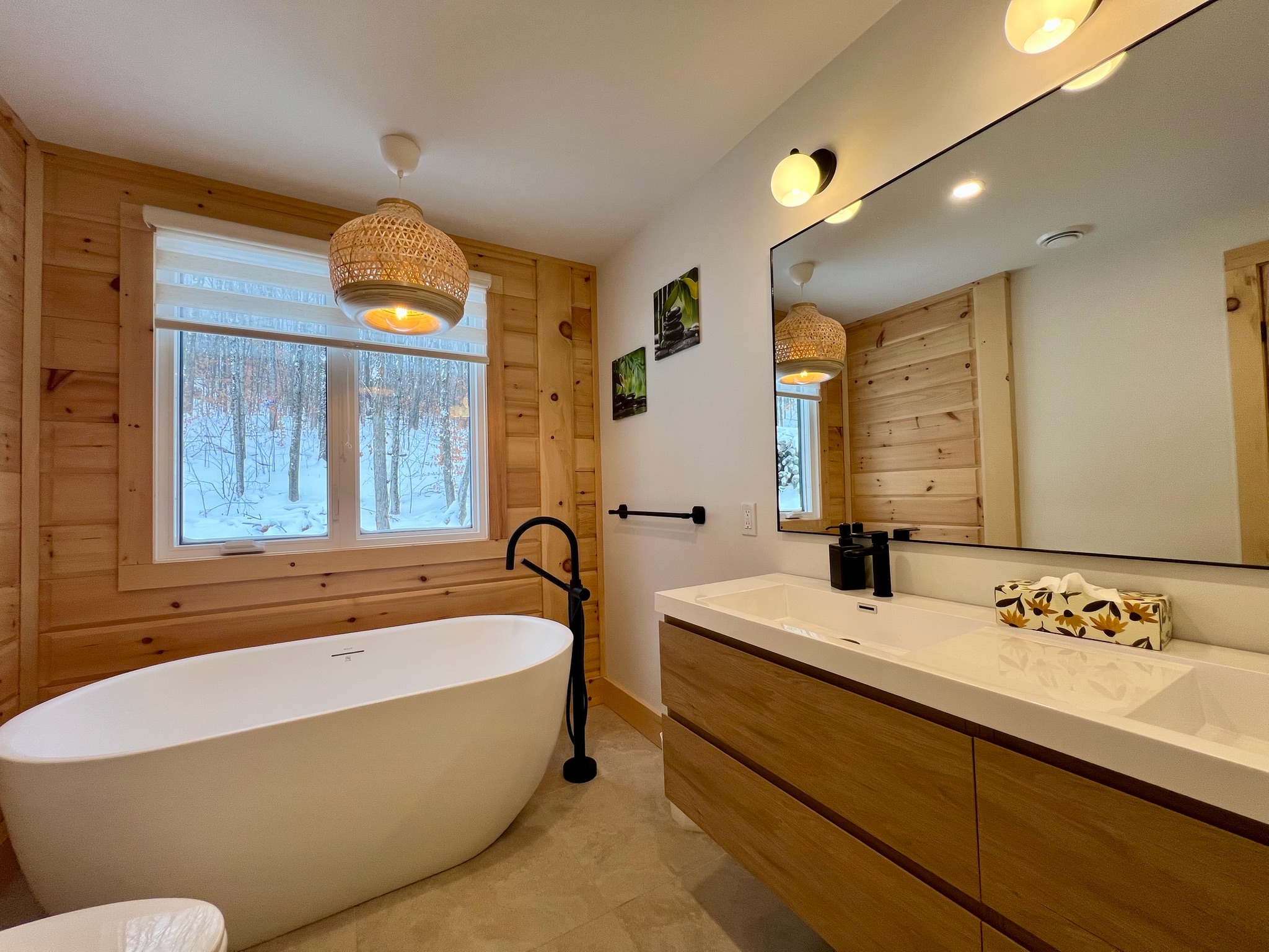 Salle de bain des maîtres avec bain autoportant, grande vanité et vue hivernale sur la forêt