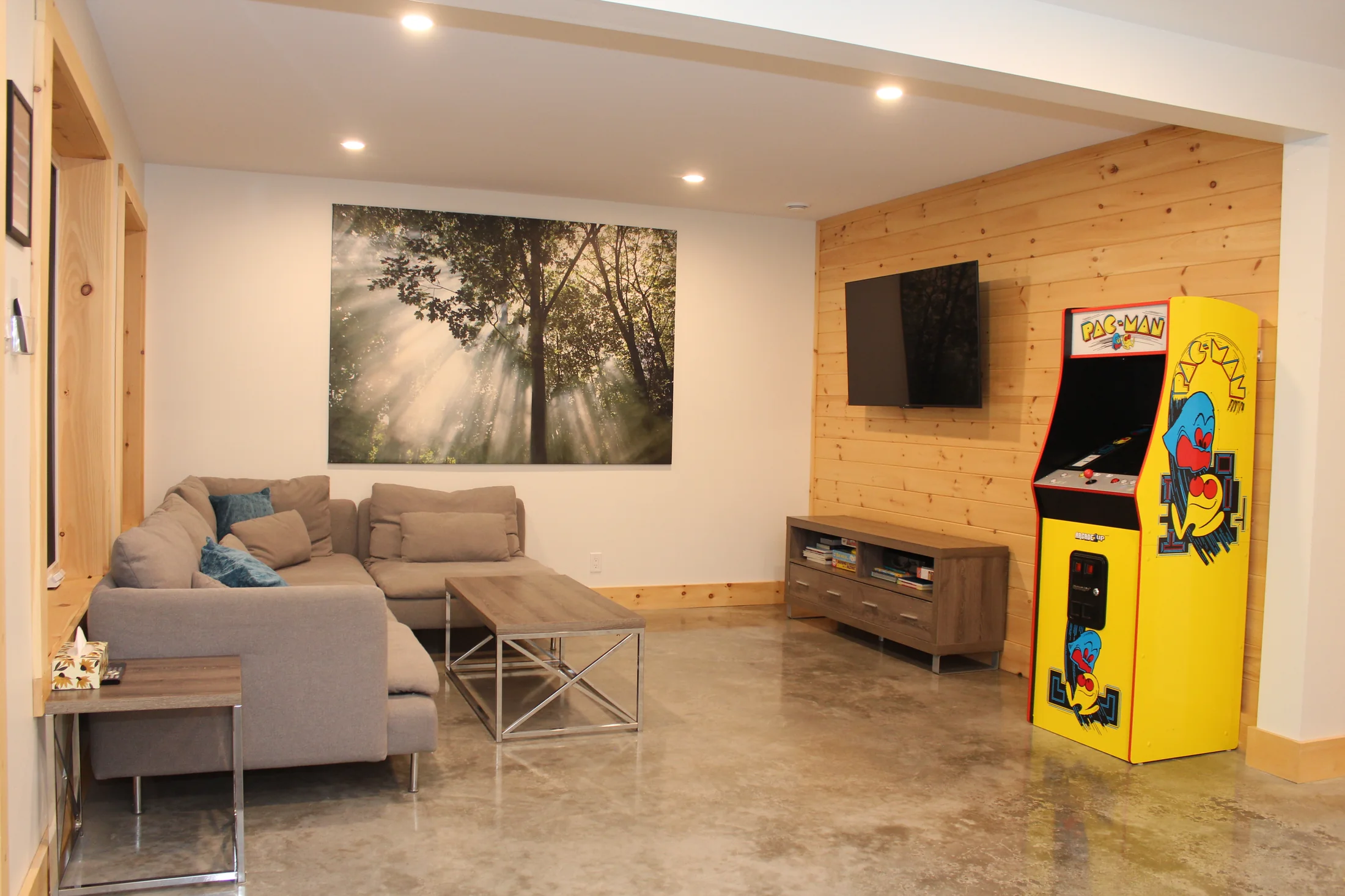 Salon du sous-sol avec grand canapé, téléviseur et borne d’arcade