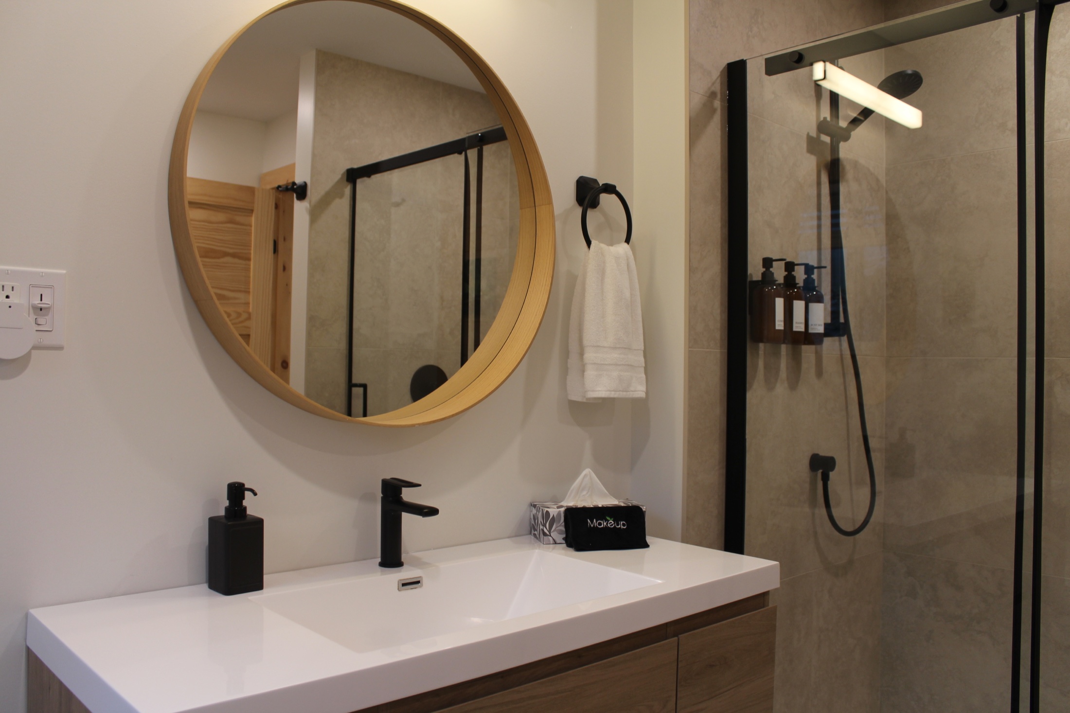 Troisième salle de bain avec meuble-lavabo, miroir rond et douche vitrée